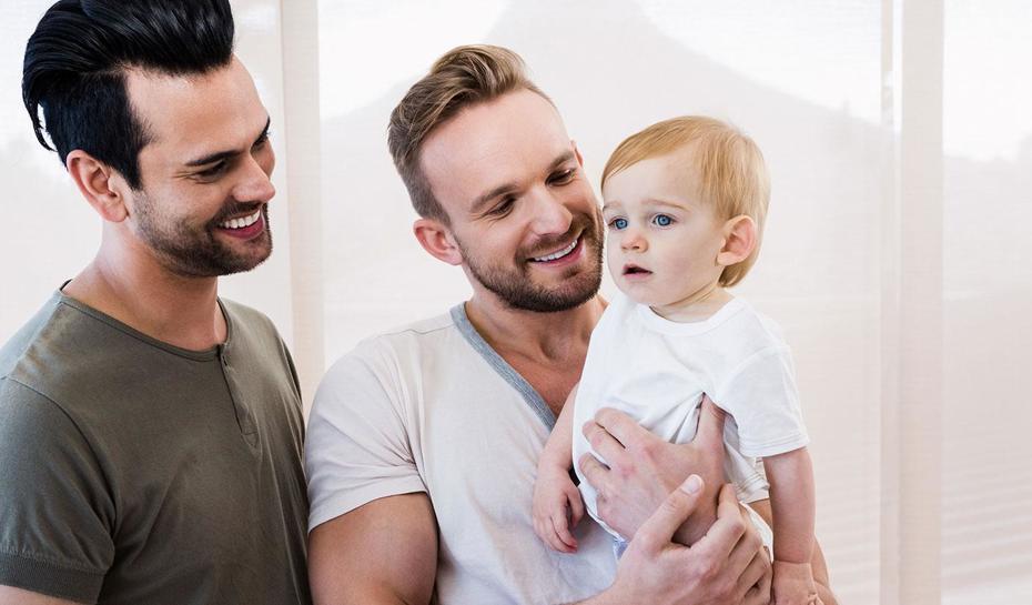 Same sex couple with one dad holding child and the other smiling